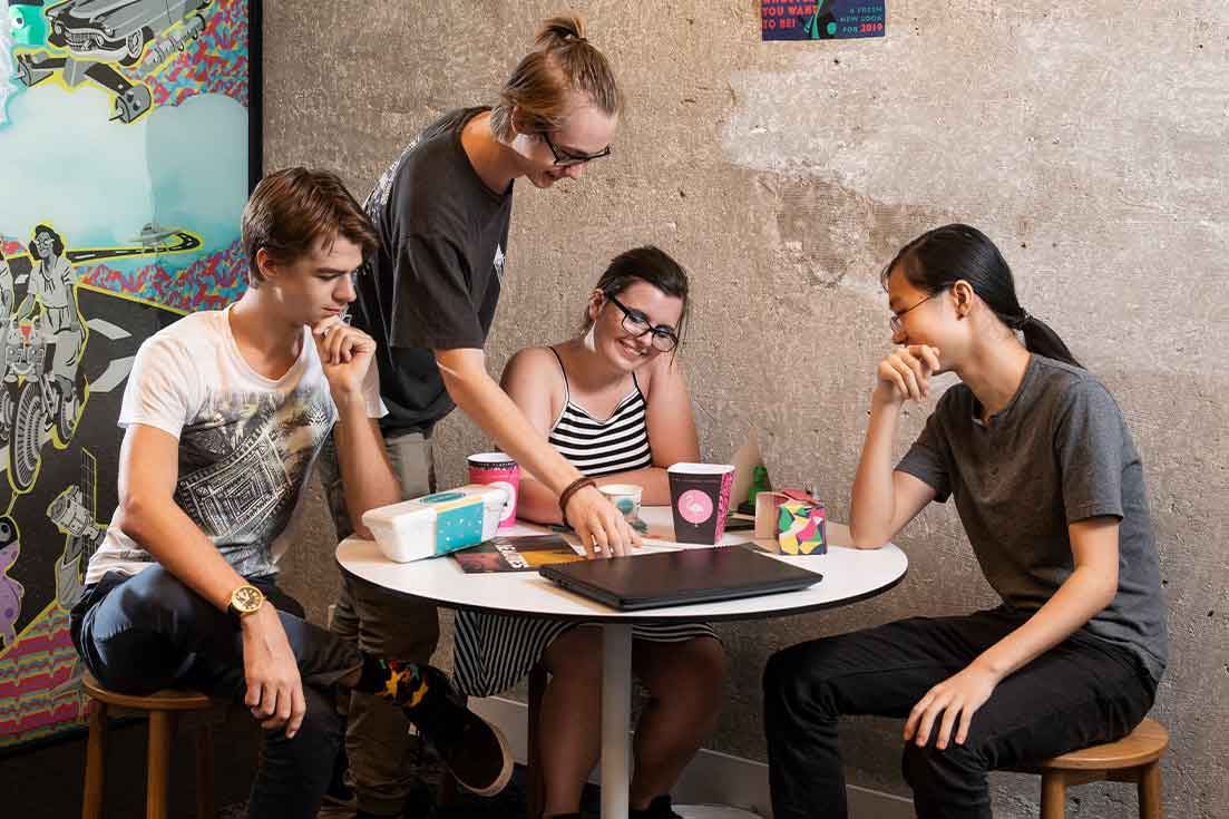 Four students sit around a desk and discuss packaging and design as a group