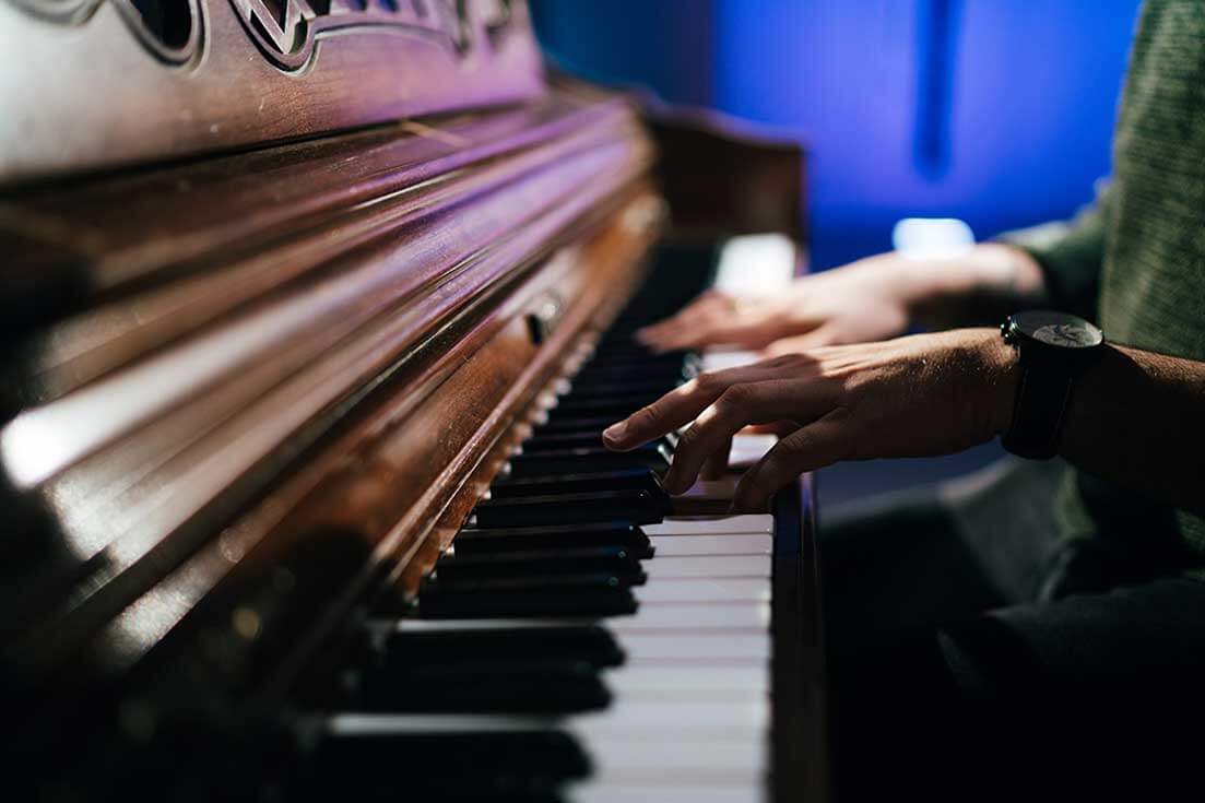 Student sits at piano and hands are placed on and playing piano