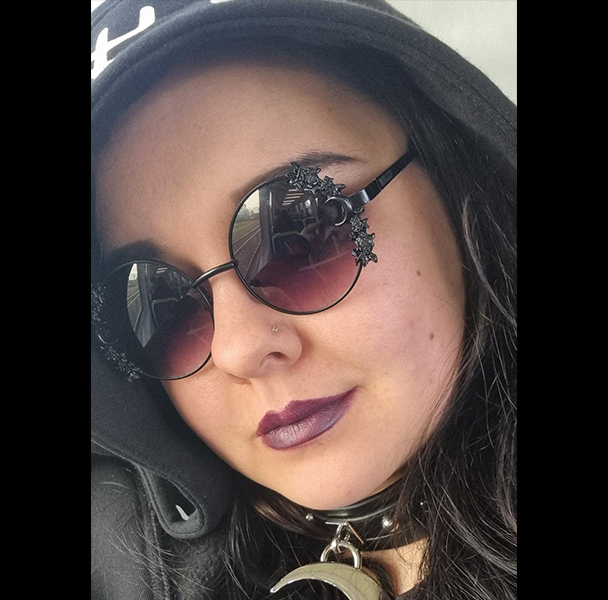 Profile photo of Zhia Zariko, wearing a black hooded jumper and crescent moon shaped choker necklace