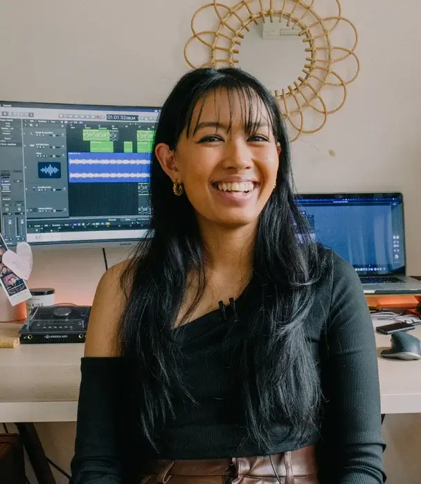 SAE AUDIO ALUMNI, AIESHA BACALSO sits in her office with her computers behind her. She smiles to camera