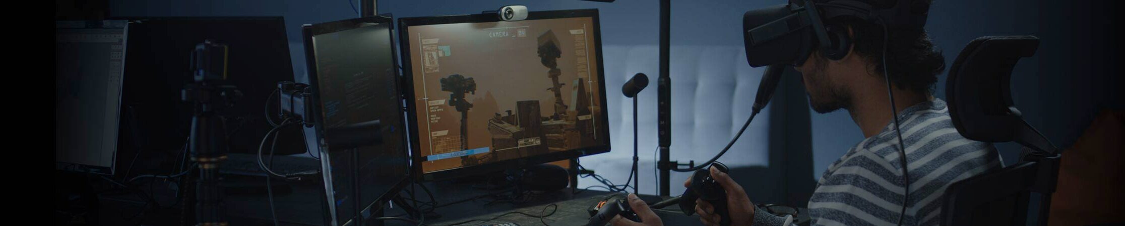 Person wearing virtual headset in front of virtual environment displayed on monitor