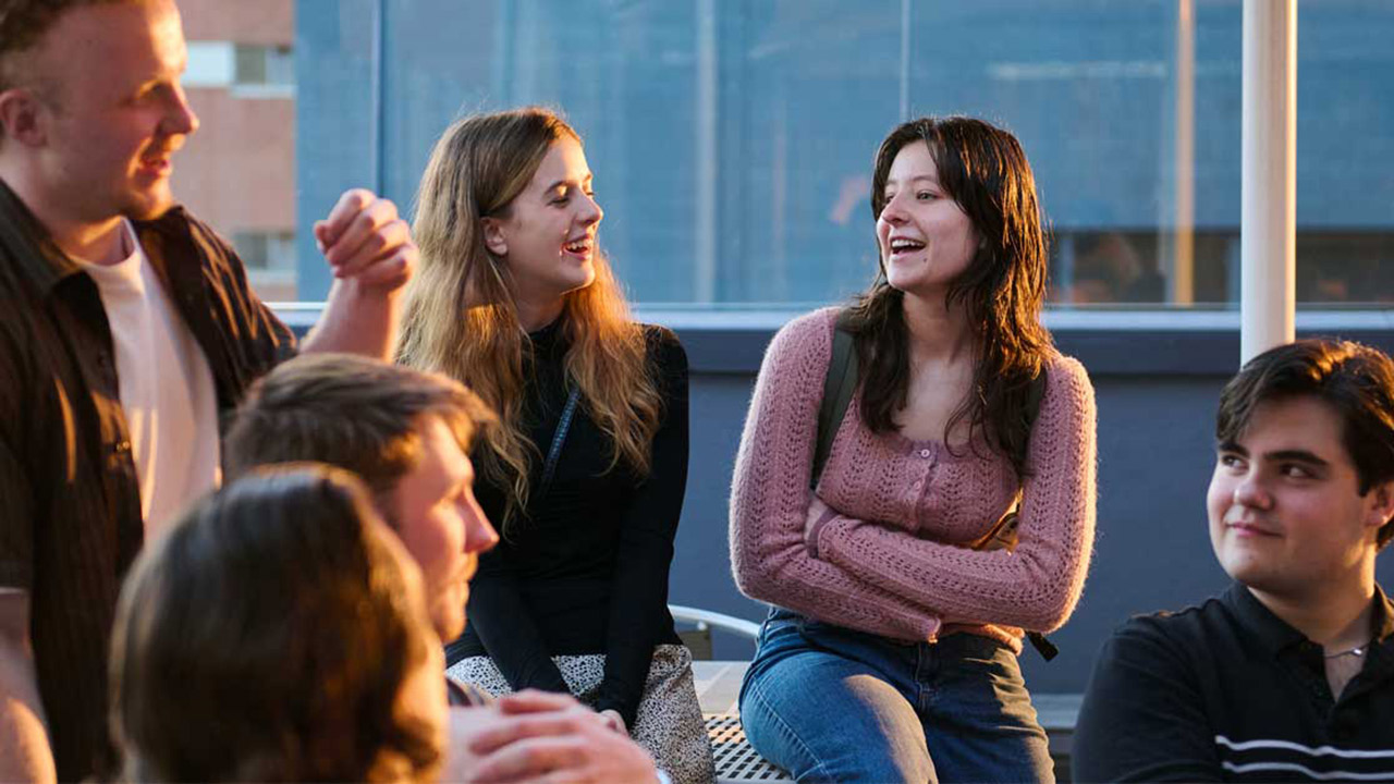Several young SAE students sitting together and smiling at an SAE University College campus
